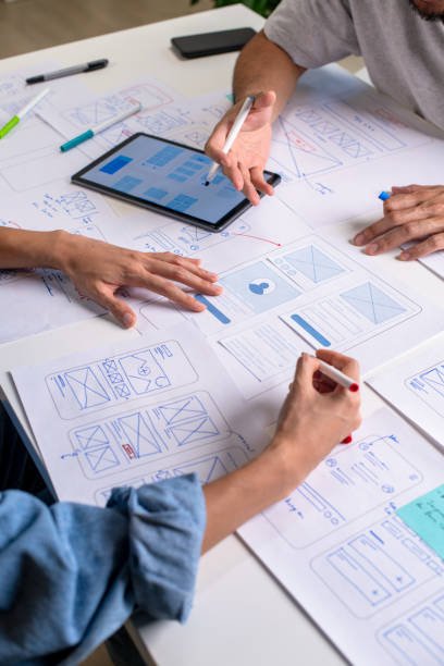 UX/UI designers discussing and brainstorming on wireframes for a website and mobile app prototype, surrounded by sketches of user flow and design tools, in the concept of website and mobile application design concept.